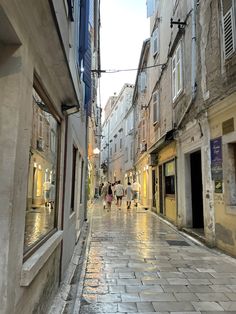 people are walking down the street in an alley way with buildings on either side and one person is holding an umbrella