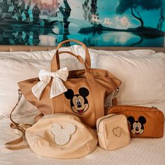 two purses and a handbag sitting on top of a bed next to each other