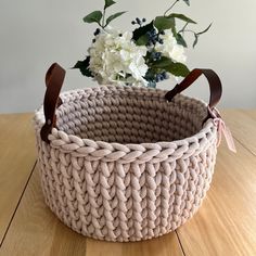 a knitted basket sitting on top of a wooden table next to a vase with flowers