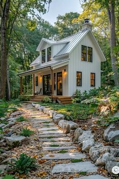 a small white house surrounded by trees and rocks in the woods with steps leading up to it