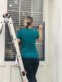 a woman standing on a stepladder in front of a window with the shutters open