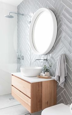 a white sink sitting under a round mirror next to a wooden cabinet in a bathroom