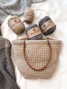 some balls of yarn sitting on top of a bed next to a crochet bag