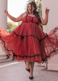 a woman in a red and black dress is walking down the street with her arms outstretched