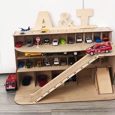 a wooden toy car garage with cars and ramps on the floor next to a wall