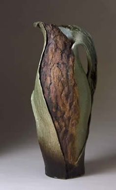 a brown and green vase sitting on top of a white table next to a gray wall