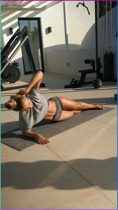 a woman laying on her stomach in the middle of a gym floor doing an exercise