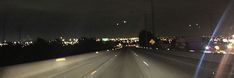 the view from inside a car driving down a highway at night with city lights in the background