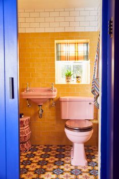 a pink toilet and sink in a small bathroom with yellow tiles on the floor,