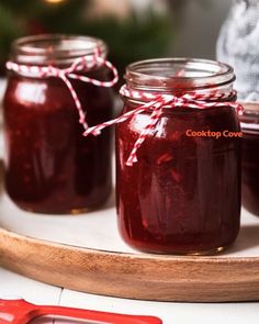 three jars filled with red liquid sitting on top of a wooden tray next to a christmas tree