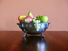 a metal bowl filled with fruit on top of a wooden table