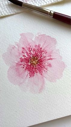 a pink flower painted on white paper next to a brush