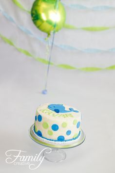 a cake with blue and green polka dots on it sitting in front of a balloon