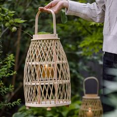 a person holding a lantern in the middle of a garden with trees and bushes behind it