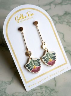 a pair of earrings sitting on top of a white and gold card with the words golden fern