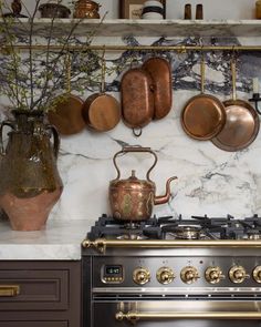 pots and pans are hanging on the wall above an oven in a kitchen with marble counter tops