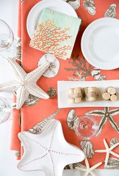 the table is set with wine glasses, plates and starfish napkins on it