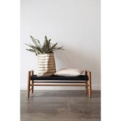 a plant sitting on top of a wooden bench next to a white wall and black cushion