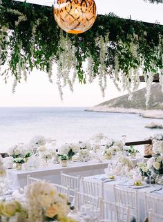 an outdoor wedding setup with white flowers and greenery hanging from the ceiling, overlooking the ocean