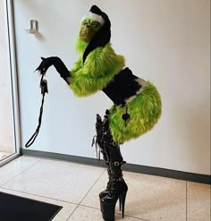 a woman dressed in green and black is standing with her legs spread out while wearing high heeled boots