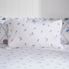 a bed with white sheets and blue flowers on the pillowcase, along with two pillows