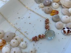 various sea glass beads and shells on a white tray with gold chains, including one bead