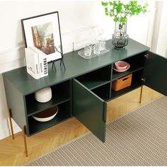 a green table with two drawers and a vase on the top, in front of a white wall