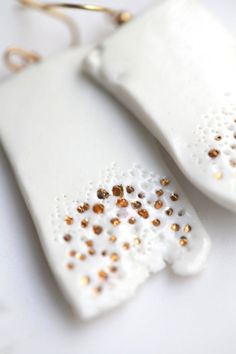 two white ceramic pieces with gold and silver beads on them sitting next to each other