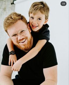 a man holding a little boy in his arms and smiling at the camera while he is wearing glasses