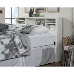 a bed with white sheets and pillows in a bedroom next to a chair, bookshelf and pictures on the wall