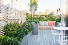 an outdoor patio with white chairs and plants on the deck, surrounded by greenery