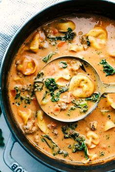 a ladle full of soup with dumplings and spinach on the side, ready to be eaten