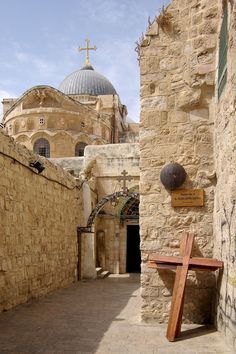 an old stone building with a wooden bench in the foreground and a cross on the wall