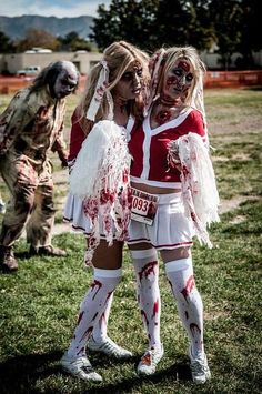 two women dressed as zombies are hugging in the grass while another woman is walking behind them