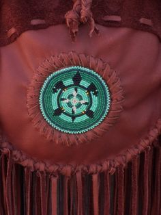 This boho fringed leather tote handbag is made is soft mahogany cowhide leather. It has fringe all around and measures 10 inches tall x 10 inches wide x 2.75 inches deep. There is an extra pocket inside. The beaded turtle totem is done mostly in shades of green glass seed beads and has a center focal of eagle feathers. There are also four directional colors inside the turtle totem. (Refer to the picture.) If you would like a different beaded rosette contact us. The beaded rosette is sewn on and Bohemian Brown Bag With Beaded Fringe, Brown Artisan Bags With Fringe, Artisan Brown Bags With Fringe, Artisan Brown Bag With Fringe, Artisan Brown Fringe Bag, Traditional Brown Fringe Bag, Artisan Brown Beaded Bag, Medicine Bag Necklace, Beaded Turtle