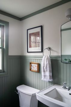 a white toilet sitting next to a bathroom sink under a framed picture on the wall