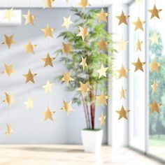 some gold stars hanging from the ceiling in front of a potted plant and window