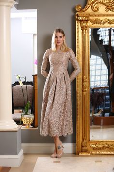 a woman standing in front of a mirror wearing a dress with long sleeves and high heels