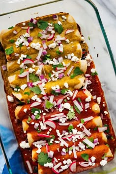 three enchiladas in a glass baking dish on a marble countertop with shredded cheese and cilantro