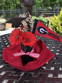 a black vase with red flowers on top of a table next to a university flag