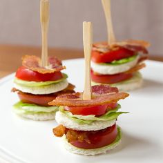 small sandwiches with bacon, lettuce and tomato on a white plate topped with toothpicks