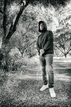 black and white photograph of man in hoodie standing on grass with trees behind him