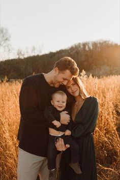 a man, woman and baby are standing in the tall grass with their arms around each other