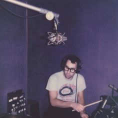 a man sitting in front of a drum set with headphones on his ears and holding a pair of drumstick