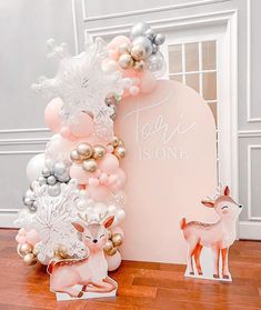 a pink and silver balloon arch with a deer figurine next to it on a wooden floor