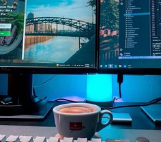 a cup of coffee sitting on top of a desk next to a computer monitor and keyboard