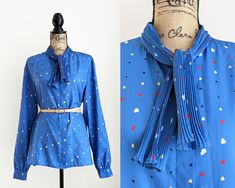 Vintage 80s blue secretary blouse with long sleeves, ridged bow ties at the collar, and an abstract graphic print. Button-down closure.  Made of lightweight silky polyester. Brand: Haberdashery by Personal Size: no size tag but estimated to be a size medium to large. Please use the measurements below to ensure an accurate fit. Fabric: polyester Condition: There is a small dark mark on the left shoulder (please see the last photo). Aside from this, the blouse is in good vintage condition. Measurements: Bust: 46" Waist: 44" Hip: 46" Length: 27" Sleeve length: 26" Shoulder (across): 18" PLEASE NOTE: All items I sell are vintage and are not new. I try my best to describe the condition of each item as accurately as possible. I highly encourage you to click on each photo in the listing to enlarg Blue Tie Neck Blouse For Fall, Vintage Blue Blouse For Fall, Retro Blue Blouse For Fall, Blue Retro Blouse For Work, Vintage Tie Neck Office Top, Retro Blue Blouse For Work, Vintage Tie Neck Blouse For Work, Retro Blue Blouse For Workwear, Vintage Tie Neck Top For Office