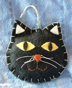 a black cat ornament hanging on a blue cloth with white stripes and yellow eyes