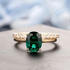 an emerald colored ring with white diamonds on the sides and gold band, sitting on top of a table