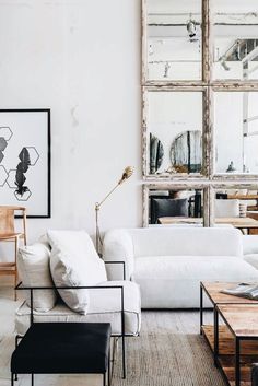 a living room filled with white couches and mirrors on the wall above them is a coffee table